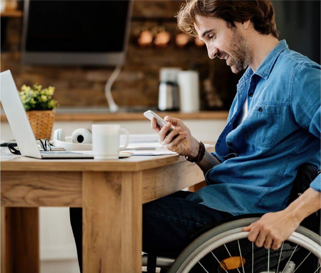 Covjek sjedi za stolom i gleda u mobitel i u laptop